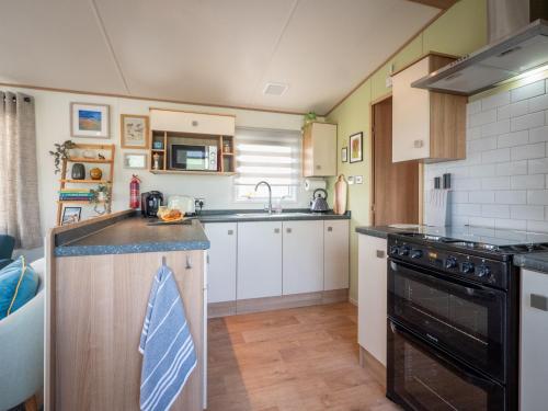uma cozinha com armários brancos e electrodomésticos pretos em Little Curlew, Ynyslas, Borth em Borth