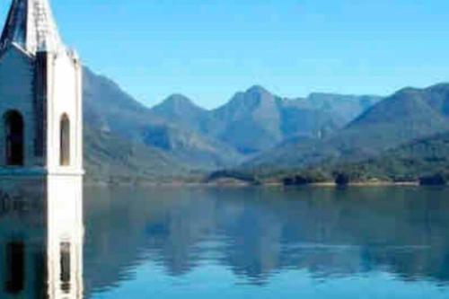 a church on a lake with mountains in the background at Aconchegante Quitinete Próximo ao Centro/Criciúma. in Criciúma