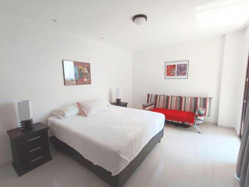 ein weißes Schlafzimmer mit einem Bett und einem roten Stuhl in der Unterkunft Monoambiente CasArte Takubamba in Santa Cruz de la Sierra