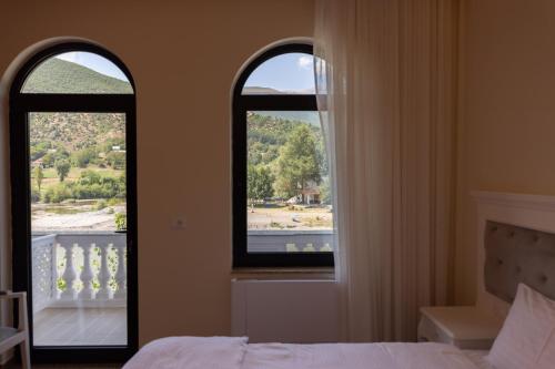 a bedroom with two windows and a bed and a balcony at Bujtina Drini i Zi in Peshkopi