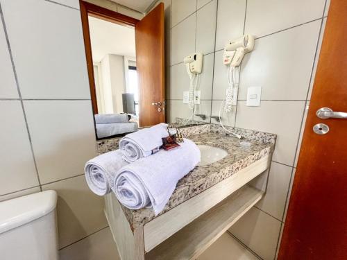 a bathroom with a sink and a mirror and towels at Janastí Suítes Praia de Ponta Negra in Natal