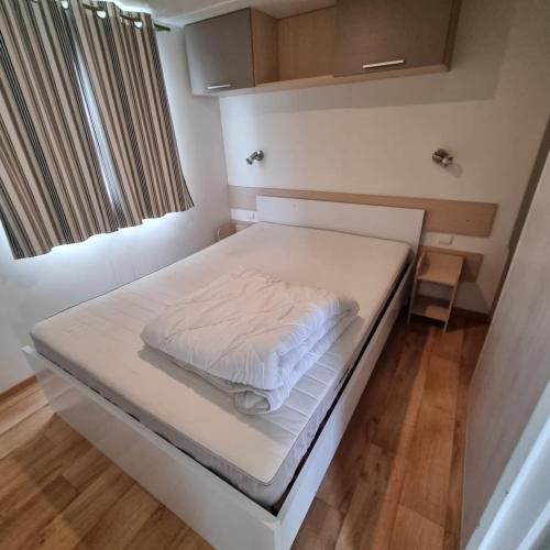een kleine slaapkamer met een bed met witte lakens bij Luxueuze stacaravan 4pers met terras en tuintje Bredene (2010) in Bredene