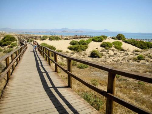 a woman walking on a wooden boardwalk over the beach at Sonido del Mar in Gran Alacant