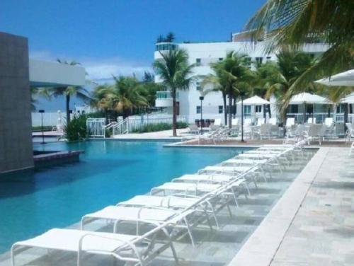 una fila de tumbonas blancas en una piscina en Resort em Natal RN à beira mar, en Parnamirim