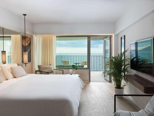 1 dormitorio con 1 cama blanca grande y balcón en NIKO Seaside Resort MGallery en Agios Nikolaos