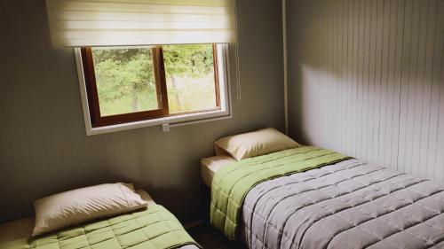 Habitación pequeña con 2 camas y ventana en Cabañas Altos de Nalhuitad, en Chonchi