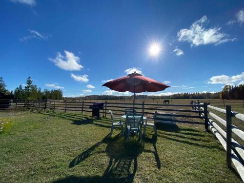 a table and chairs with an umbrella in front of a fence at Woodhouse Cottages And Ranch in Prince George