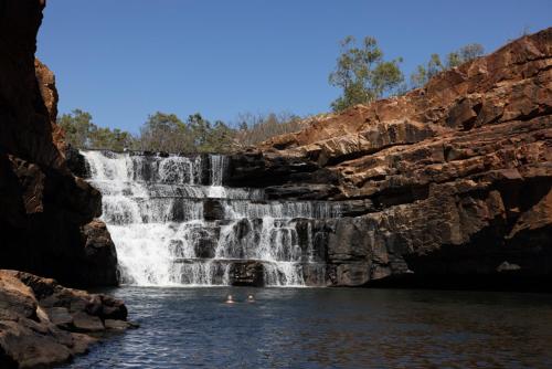 a waterfall in a river with people swimming in it at Bell Gorge Wilderness Lodge in King Leopold Ranges