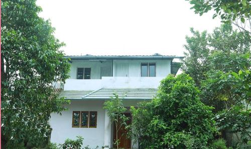 una casa blanca con árboles delante de ella en Blooms home stay, en Thekkady