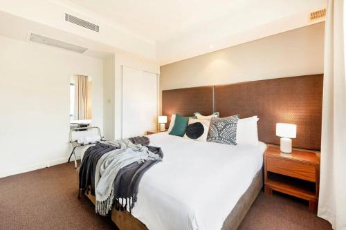 a bedroom with a large white bed and a wooden headboard at Poolside Resort Living on Esplanade with Balcony in Darwin