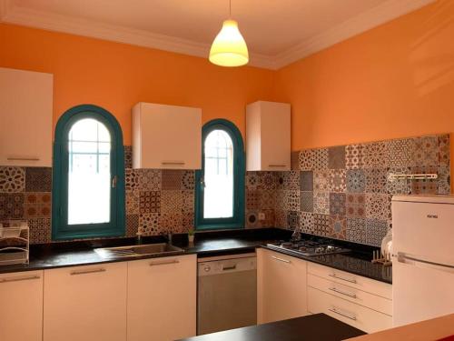 eine Küche mit orangefarbenen Wänden, weißen Schränken und Fenstern in der Unterkunft Spacious 3-Floor Riad in Marrakesch