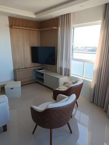 sala de estar con 2 sillas y TV de pantalla plana en Incrível Vista Panorâmica, en Tramandaí