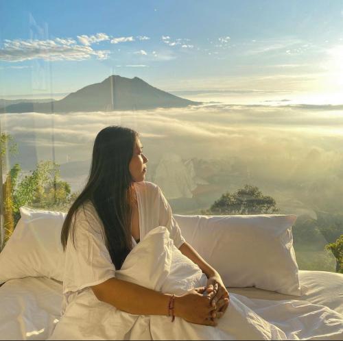 a woman sitting on a bed with a view of a mountain at Devanora Hotel & Resto in Kintamani
