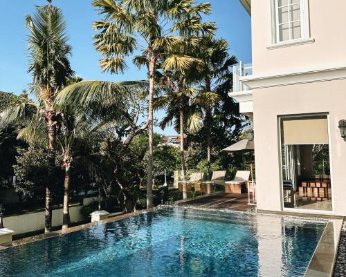 a swimming pool in front of a house with palm trees at Kula Kara Villas Uluwatu in Uluwatu