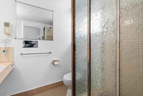 a bathroom with a toilet and a glass shower door at Commodore Motor Inn in Albury