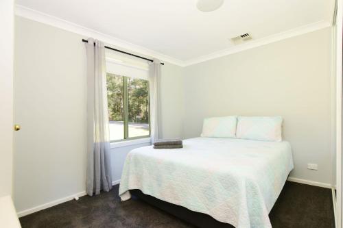 a white bedroom with a bed and a window at Beau Villa - Two bedroom Villa on golf course in Kangaroo Valley