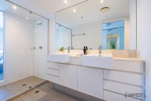 a white bathroom with two sinks and a shower at Gorgeous 2BR Apt with City & Water views Southport in Gold Coast
