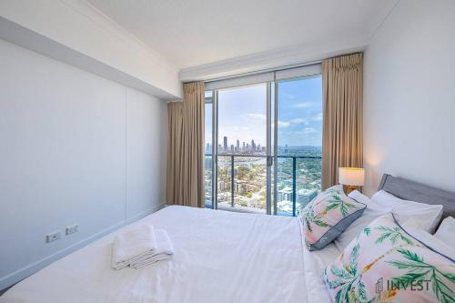 um quarto com uma cama branca e uma grande janela em Gorgeous 2BR Apt with City & Water views Southport em Gold Coast