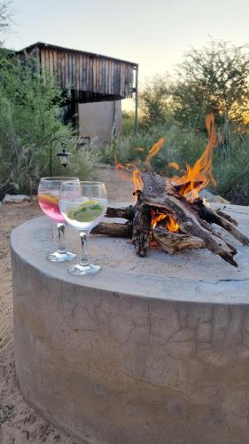 a glass of wine sitting on a table next to a fire at Hackberry House Bushwillow Cottage (Off Grid) in Khemsbok