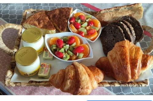 uma bandeja de alimentos de pequeno-almoço com croissants, frutas e pão em Chambre d hôte Beaumont pied de bœuf em Beaumont-Pied-de-Boeuf