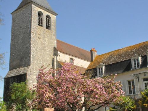 una iglesia con una torre y un árbol con flores rosas en Le Prieuré Saint Agnan, en Cosne-Cours-sur-Loire