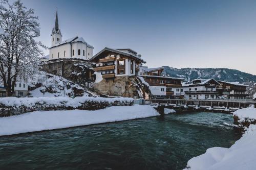 a river in front of a town with snow covered buildings at Margarethenstein Boutique Hotel in Kaprun