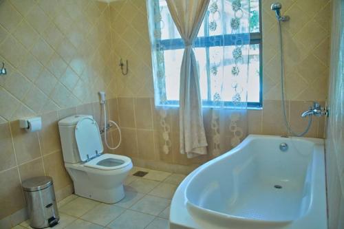 La salle de bains est pourvue de toilettes, d'une baignoire et d'une fenêtre. dans l'établissement UPENDO SAFARI LODGe, à Karatu