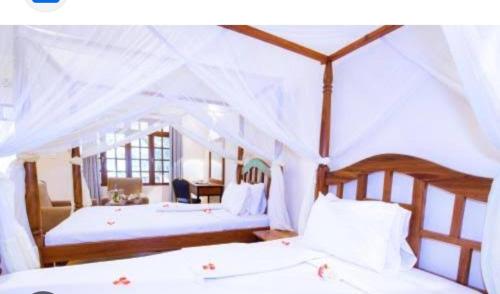 1 dormitorio con 2 camas con sábanas blancas en UPENDO SAFARI LODGe en Karatu
