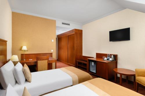 a hotel room with two beds and a television at Mercure Szekesfehervar Magyar Kiraly in Székesfehérvár