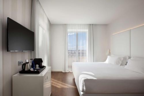 a white bedroom with a bed and a television at NH Madrid Atocha in Madrid