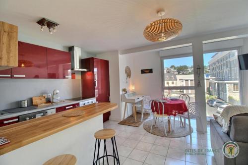 - une cuisine et un salon avec des armoires rouges et une table dans l'établissement Studio du phare, à Perros-Guirec