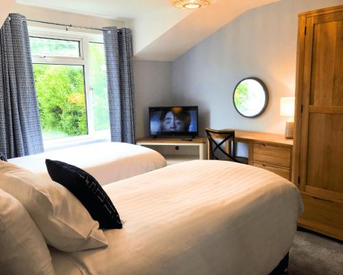 two beds in a room with a television and a desk at Harbourmaster Hotel in Aberaeron