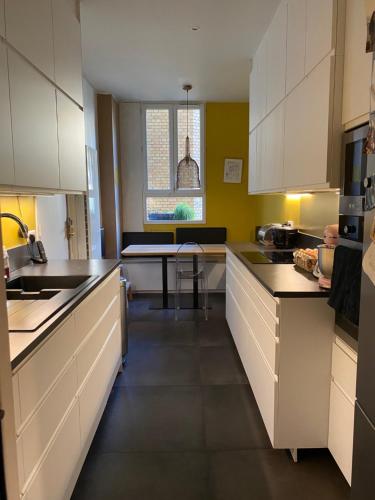 une cuisine avec des armoires blanches et une table à l'intérieur dans l'établissement Paris, grand appartement familial, porte Maillot, à Neuilly-sur-Seine