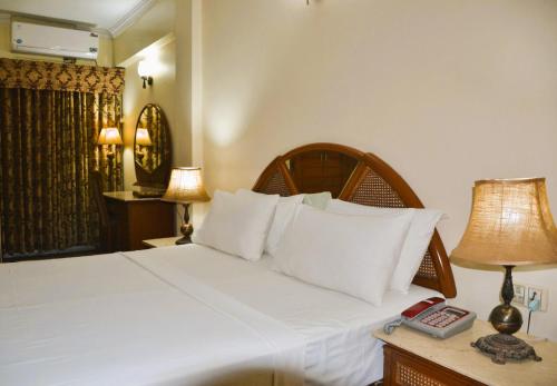 een slaapkamer met een bed met witte lakens en een lamp bij Pak Continental Hotel in Bahawalpur