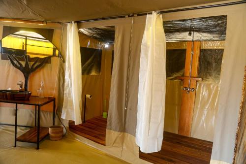Habitación con ducha, cortinas y lámpara. en Ndoto Serengeti Camp en Serengeti