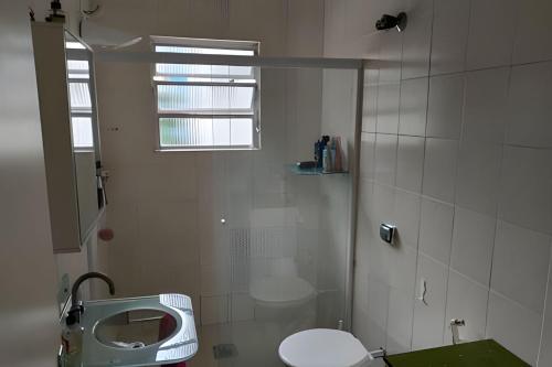 La salle de bains blanche est pourvue de toilettes et d'une fenêtre. dans l'établissement Apartamento em Guarujá a 200 m da Asturias e Tombo, à Guarujá