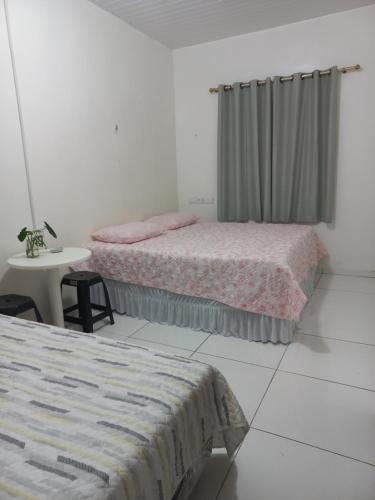 two beds in a white room with a table and a window at Pousada Residencial acochego caririense in Juazeiro do Norte