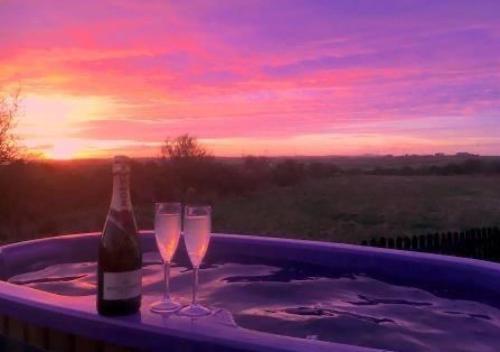 een fles champagne en twee glazen in een bad bij Glamping Huts x 3 and a Static Caravan available each with a Private Hot Tub, FirePit, BBQ and are located in a Peaceful setting with Alpacas and gorgeous countryside views on Anglesey, North Wales in Amlwch
