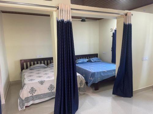 2 camas en un dormitorio con cortinas azules en Nisarga Homestay, en Gokarna