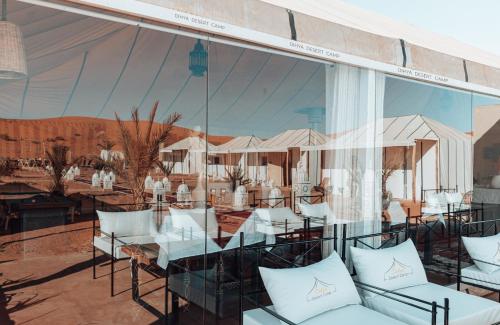 a restaurant with white tables and chairs and a large window at Dihya desert camp in Merzouga