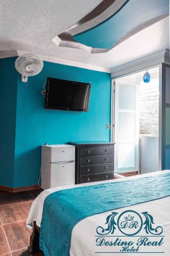 アラウカにあるDestino real hotelの青い壁にテレビとベッドが備わるベッドルーム1室が備わります。