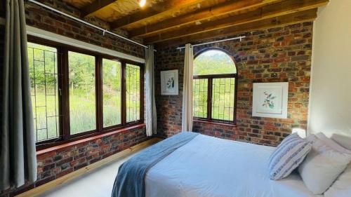 Dormitorio con paredes de ladrillo, cama y ventanas en Zens Paradise Self Catering Cottage, en Wittedrif