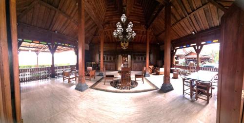 Großes Zimmer mit einem Kronleuchter sowie Tischen und Stühlen. in der Unterkunft Joglo Wismono Prambanan in Prambanan