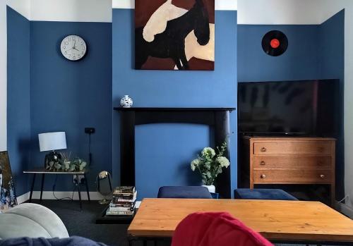 切爾滕納姆的住宿－5-Bedroom Townhouse - Ideal for Groups, Families or Contractors by Glos Homes Ltd，客厅拥有蓝色的墙壁,配有桌子和时钟