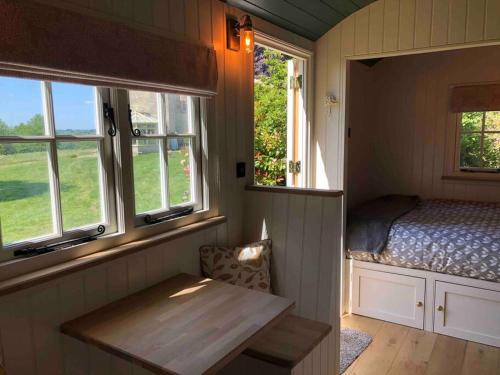 a room with a bed and a table and windows at The Old Vicarage Shepherd's Hut in Stroud