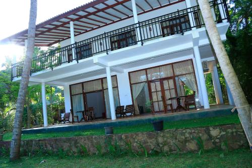 a house with a balcony and tables and chairs at River Edge Yala in Tissamaharama