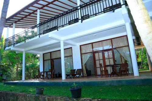 a white house with a balcony and tables and chairs at River Edge Yala in Tissamaharama
