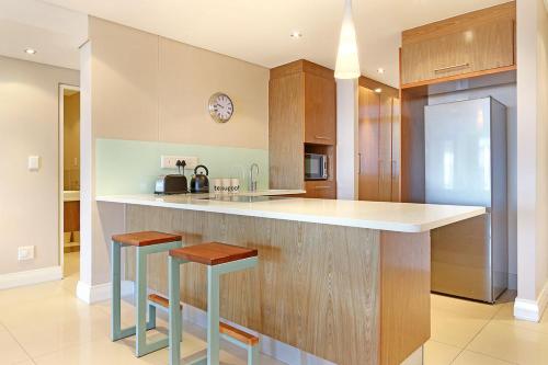 a kitchen with wooden cabinets and a counter with stools at Eden On The Bay 172 by HostAgents in Bloubergstrand