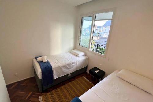um pequeno quarto com 2 camas e uma janela em Lar da Abundância: Apartamento 3 Quartos no Leblon no Rio de Janeiro