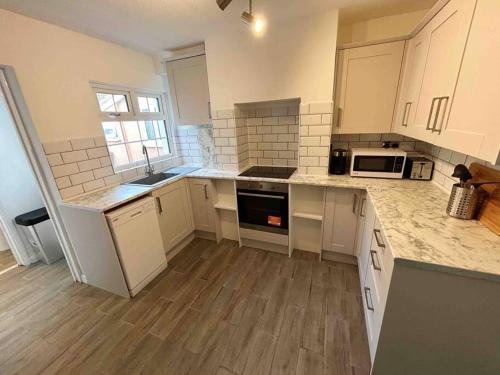 a kitchen with white cabinets and a wooden floor at Essex 2-Bed House nr Stanstead with Arcade Machine in Braintree
